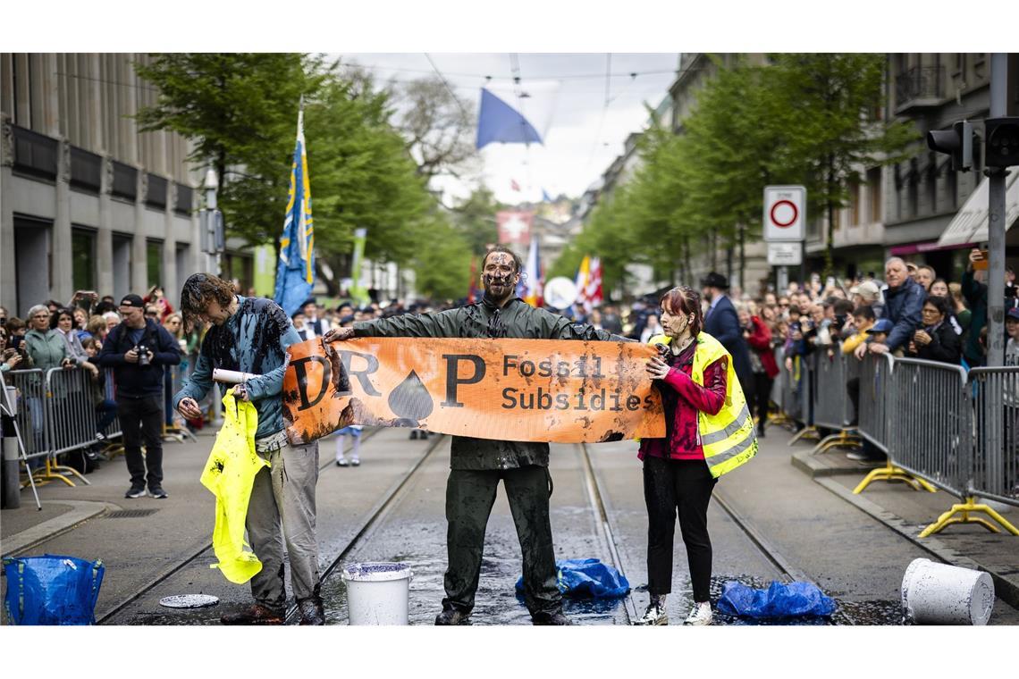 Aktivisten protestieren während des traditionellen Umzugs der Zünfte beim Sechseläuten in Zürich gegen Subventionen für fossile Brennstoffe. Um ihre Botschaft zu verdeutlichen, begießen sie sich mit einer schwarzen Flüssigkeit.