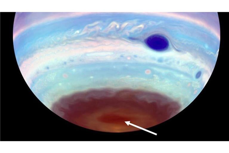 An den Polen des Jupiter haben Astronomen nur im UV-Licht sichtbare dunkle Ovale entdeckt – erdgroße, magnetisch angetriebene Tornados (Pfeil). Der Große Rote Fleck des Gasplaneten erscheint in dieser kolorierten UV-Aufnahme dunkelblau.