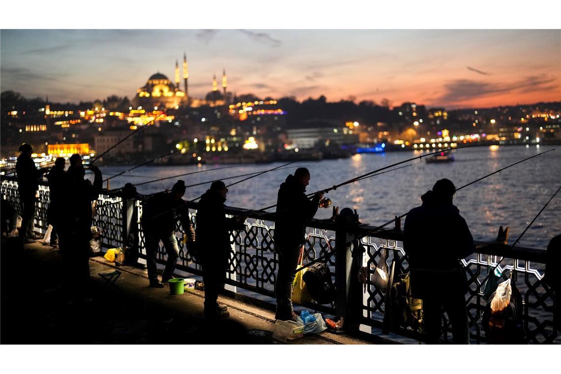 Angler in Istanbul fischen nach frischem Fisch bei Sonnenuntergang auf der Galata-Brücke über den Bosporus.