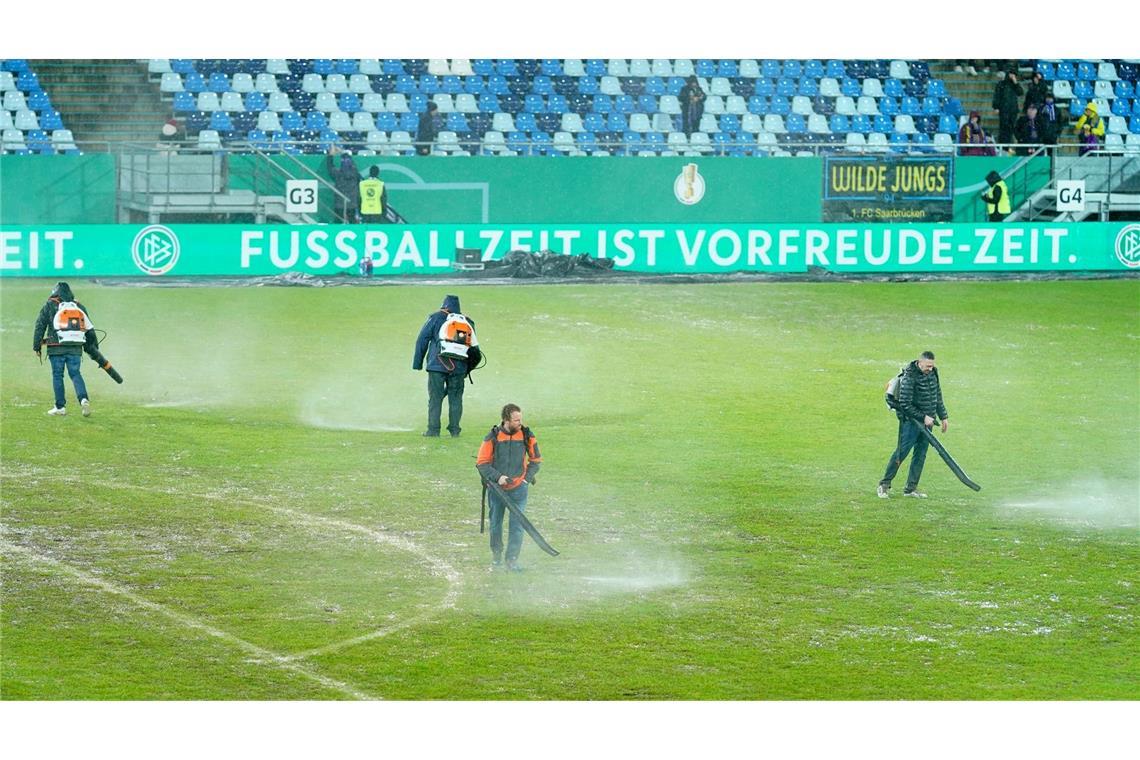 Arbeiter versuchten, Wasserlachen vom Spielfeld im Ludwigsparkstadion zu entfernen.
