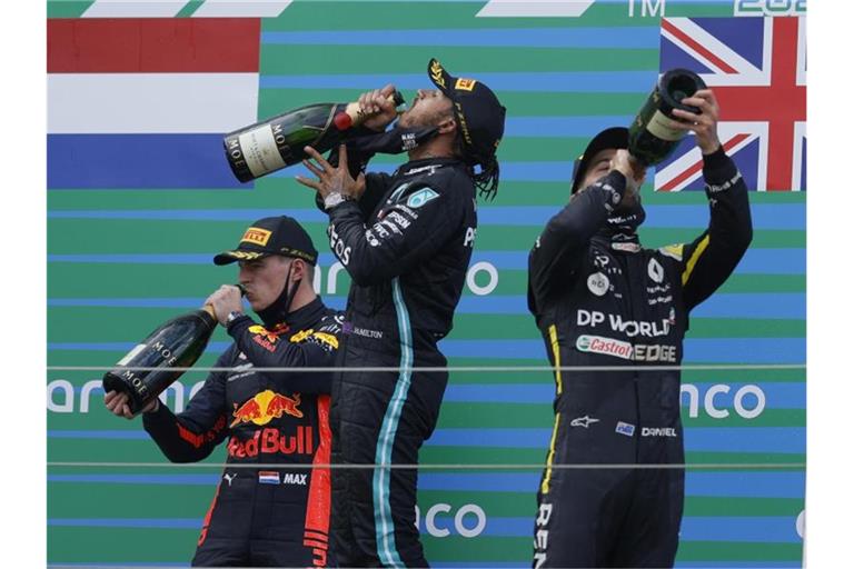 Auf dem Podest genehmigen sich der Zweitplatzierte Max Verstappen (l-r), Sieger Lewis Hamilton und Daniel Ricciardo zunächst einen großen Schluck. Foto: Ronald Wittek/Pool EPA/AP/dpa