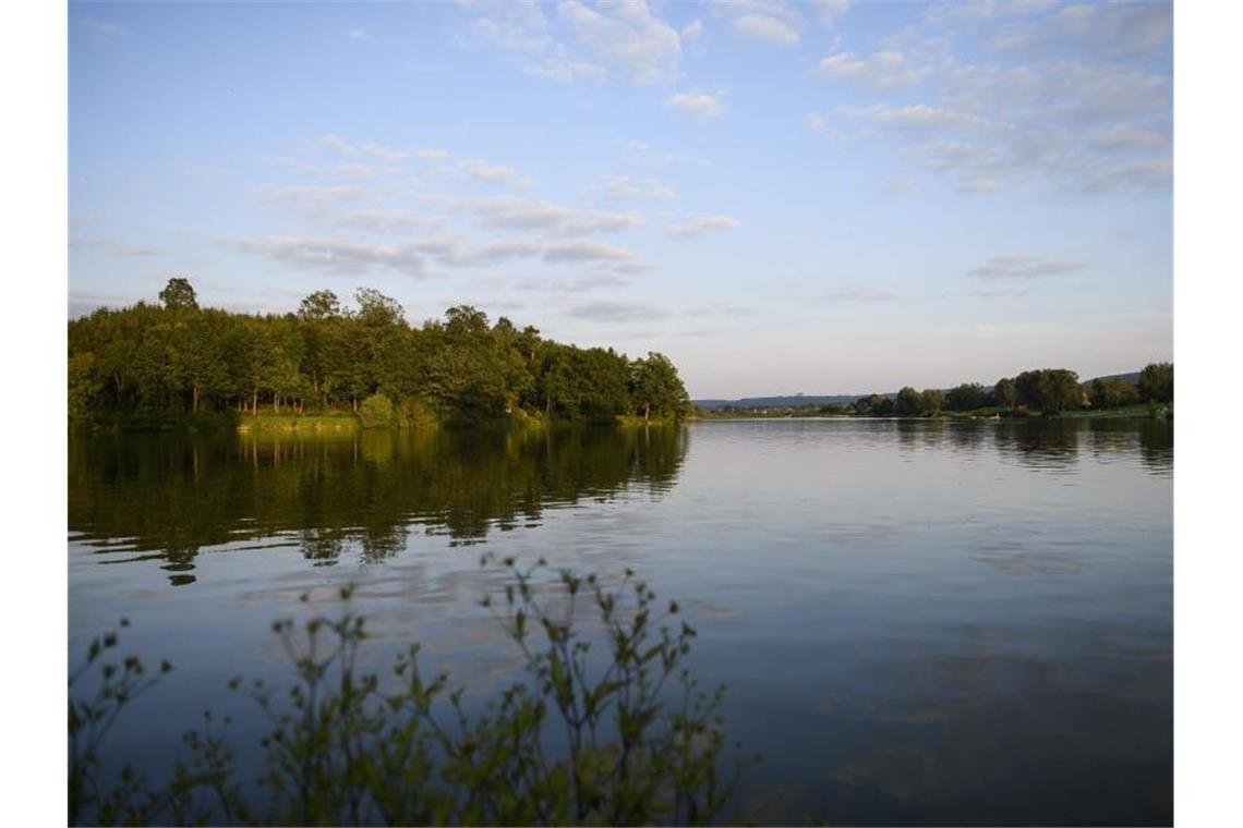 Bäume und Wolken spiegeln sich am Abend im Bucher Stausee. Foto: Edith Geuppert/dpa/Archiv