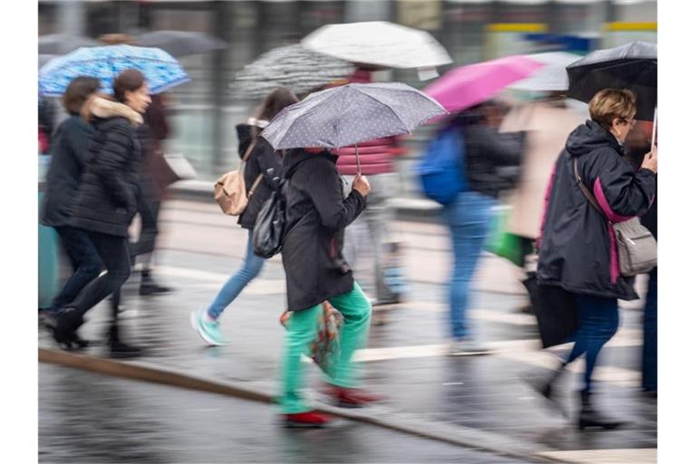 Bei Regenwetter überqueren Passanten eine Straße. F. Foto: Frank Rumpenhorst/dpa