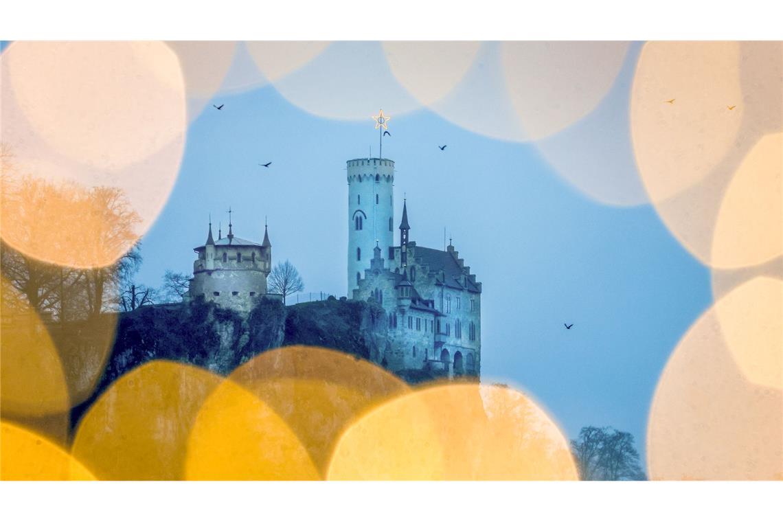 Blick am Morgen bei regnerischem Wetter durch eine Lichterkette auf das Schloss Lichtenstein auf der Schwäbischen Alb.