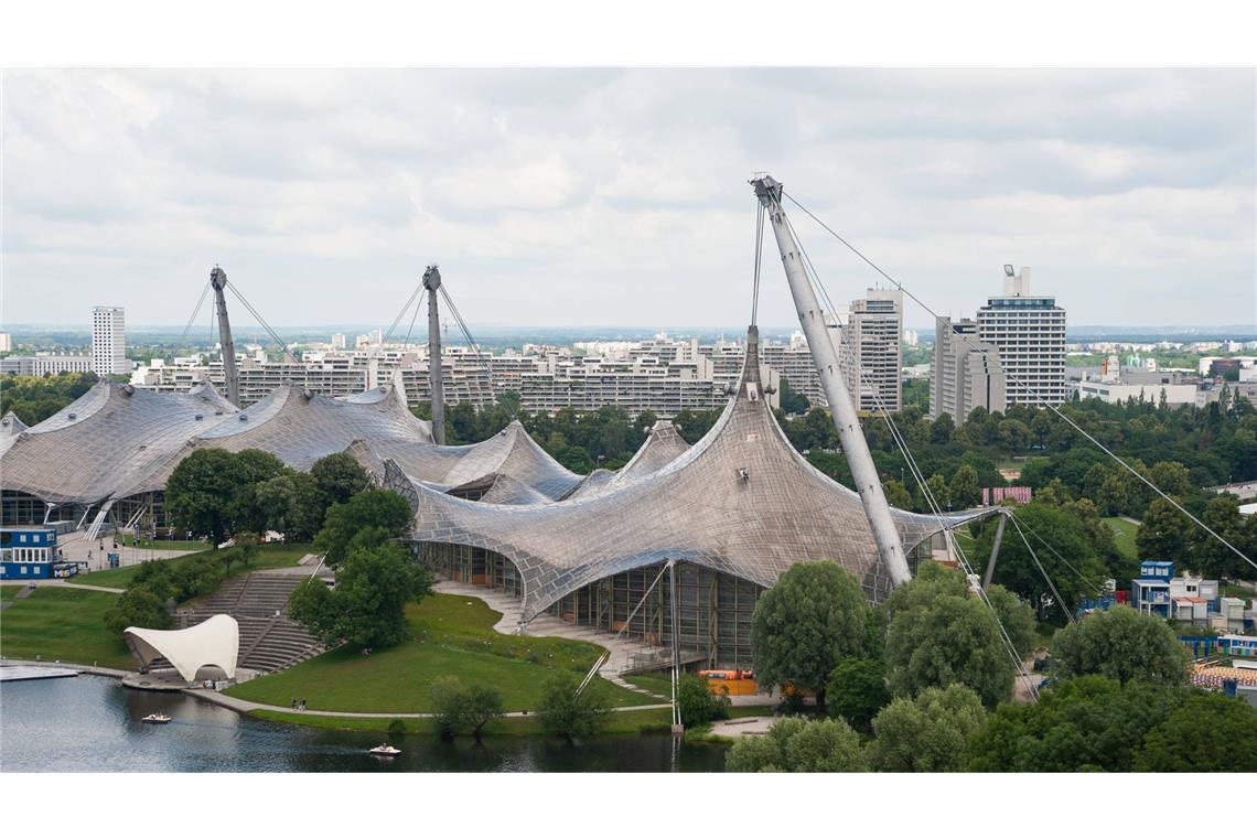 Blick vom Aussichtspunkt Olympiaberg auf die Olympia-Schwimmhalle und den Olympiasee im Olympiapark mit dem Olympiadorf im Hintergrund. Nachdem München 1966 den Zuschlag zur Austragung der XX. Olympischen Sommerspiele erhalten hatte, wurde nach einem Standort für die Sportstätten gesucht. Die Wahl fiel auf das etwa 3 km‘ große Oberwiesenfeld, das reichlich Gestaltungsmöglichkeiten bot. Als Konzept wurde „Olympische Spiele im Grünen“ (genauer: Spiele im Grünen, Spiele der Freiheit, Spiele von menschlichem Maß) gewählt, gleichzeitig wollte man sich an den Idealen der Demokratie orientieren.Für die Gestaltung wurde ein Wettbewerb ausgeschrieben, von denen der Beitrag unter der Leitung von Günter Behnisch den ersten Platz belegte. Die Architektengruppe Olympiapark, bestehend   . . .