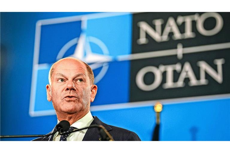 Bundeskanzler Olaf Scholz  vor dem Emblem der Nato