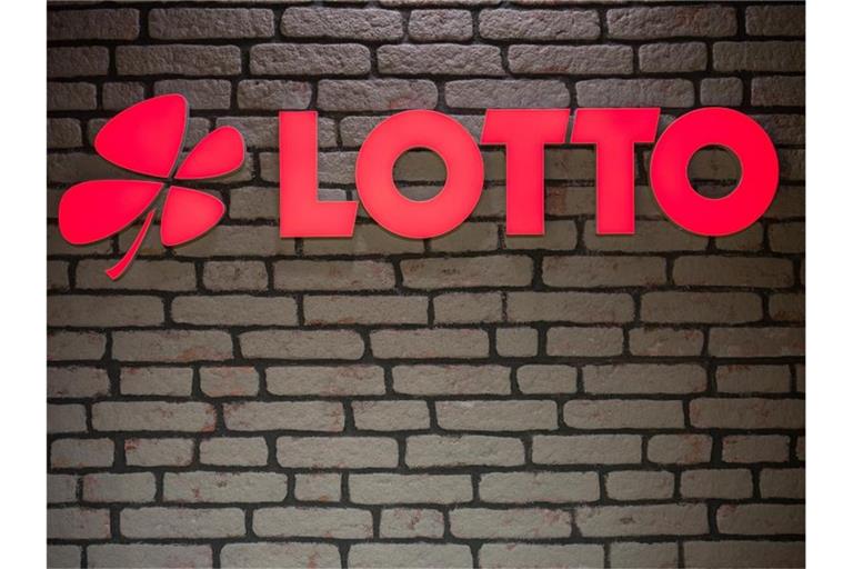 Das Lotto Logo leuchtet an einer Wand. Foto: Oliver Dietze/dpa