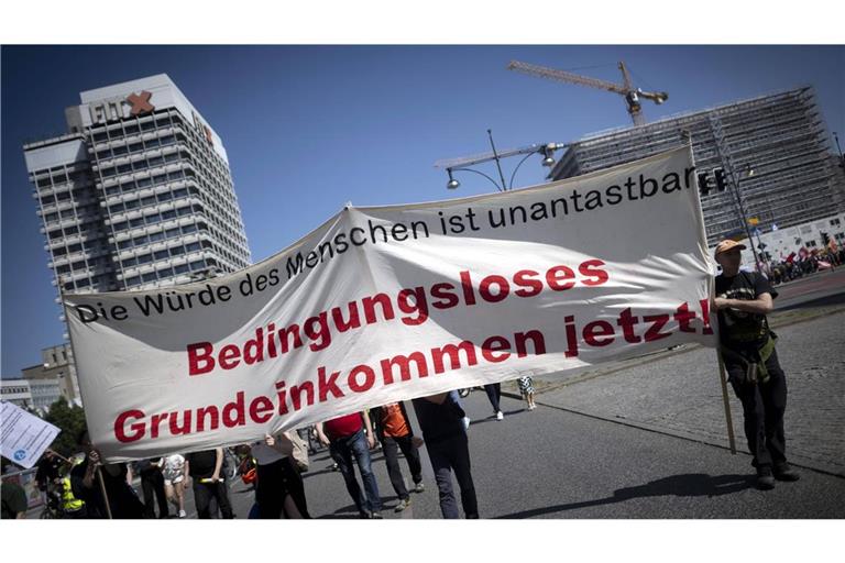 Demonstranten halten am 1. Mai 2024 in Berlin eine Transparent mit der Forderung nach einem   Bedingungsloses Grundeinkommen hoch