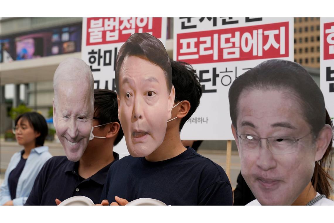 Demonstranten tragen Masken mit dem Gesicht von US-Präsident Joe Biden (l.), des südkoreanischen Präsidenten Yoon Suk Yeol (M.) und des japanischen Premierministers Fumio Kishida. Ihr Protest richtet sich gegen das Militärbündnis zwischen Südkorea, den USA und Japan.