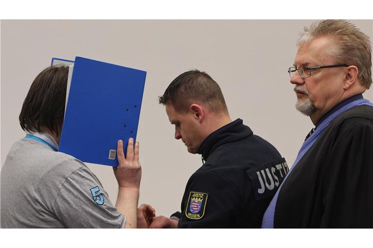 Der Angeklagte verbirgt sein Gesicht hinter einem Aktenordner und bekommt vor dem Prozess im Beisein seines Verteidigers Henner Maaß (r.) von einem Justizmitarbeiter die Handschellen abgenommen (Archivfoto).