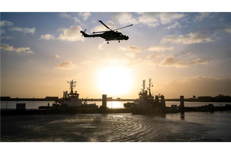 Die Besatzung eines Bundeswehrhubschraubers winkt Angehörigen, die am Pier des Marinestützpunktes in Wilhelmshaven auf die "Hamburg" warten