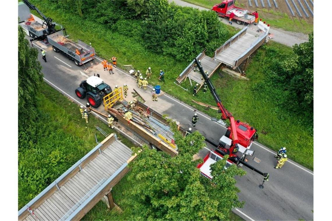 Die Feuerwehr Meckenbeuren hebt mit einem Kran einen Teil der zerstörten Brücke an, um sie auf einen Anhänger zu laden. Foto: Felix Kästle/dpa