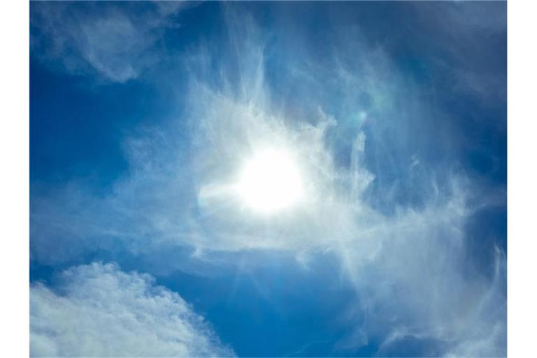 Die Sonne scheint am Himmel durch Wolken hindurch. Foto: Markus Scholz/dpa/Symbolbild