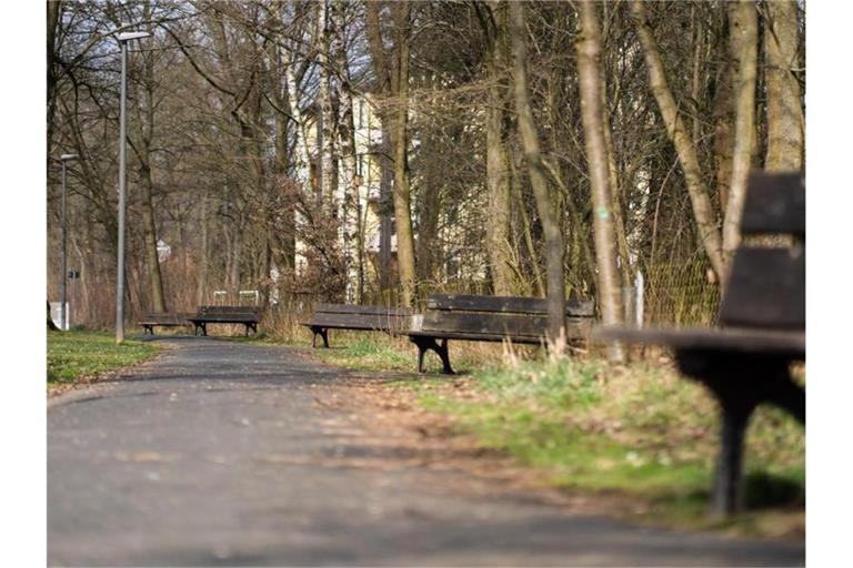 Die Sonne scheint auf leere Sitzbänke entlang eines Fußgängerweges. Foto: Nicolas Armer/dpa/Symbolbild