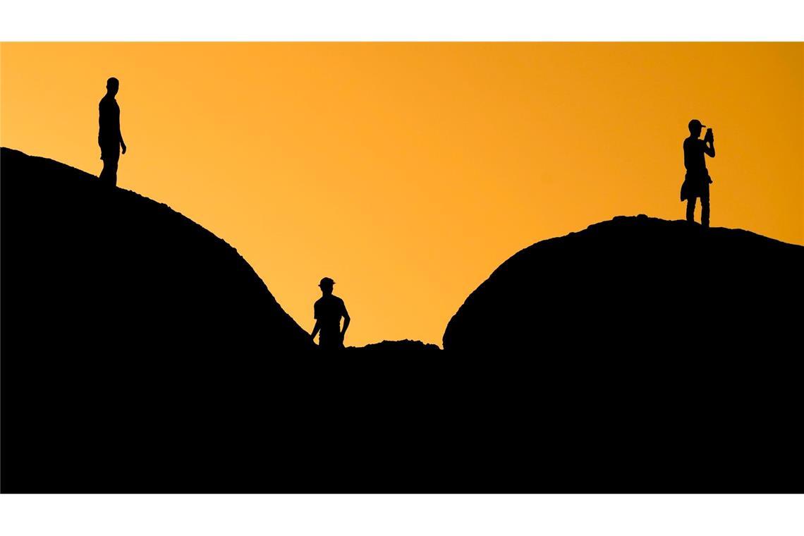 Drei Personen lassen in Arizona bei Sonnenuntergang den Tag ausklingen - dabei heben sie sich schwarz auf großen Felsen im Papago Park in Phoenix ab.