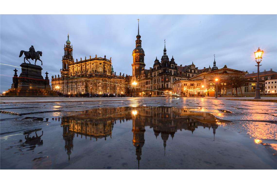 Dresden am Abend - Das Reiterstandbild König Johann (l-r), die Hofkirche, der Hausmannsturm, das Residenzschloss und die Schinkelwache spiegeln sich am Abend in einer Pfütze auf dem Theaterplatz.