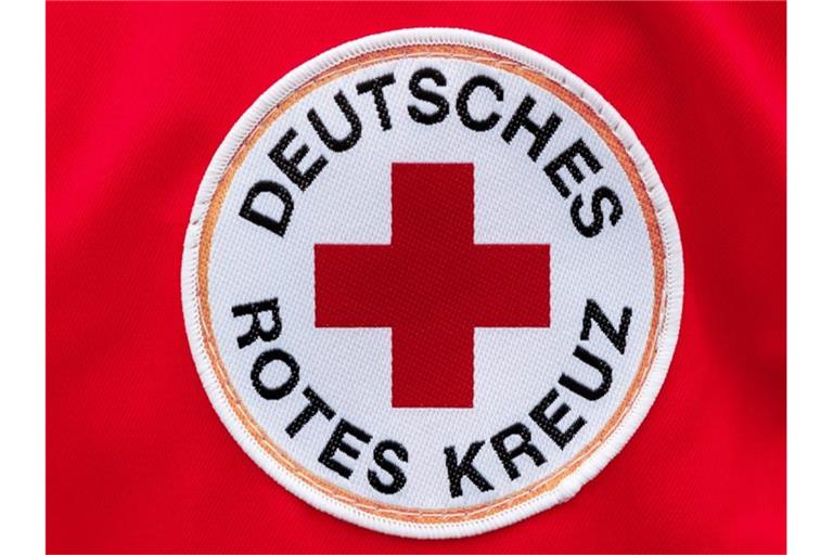 Ein Aufnäher mit dem Logo des Deutschen Roten Kreuzes (DRK) ist auf rotem Hintergrund zu sehen. Foto: Markus Scholz/dpa/Archivbild