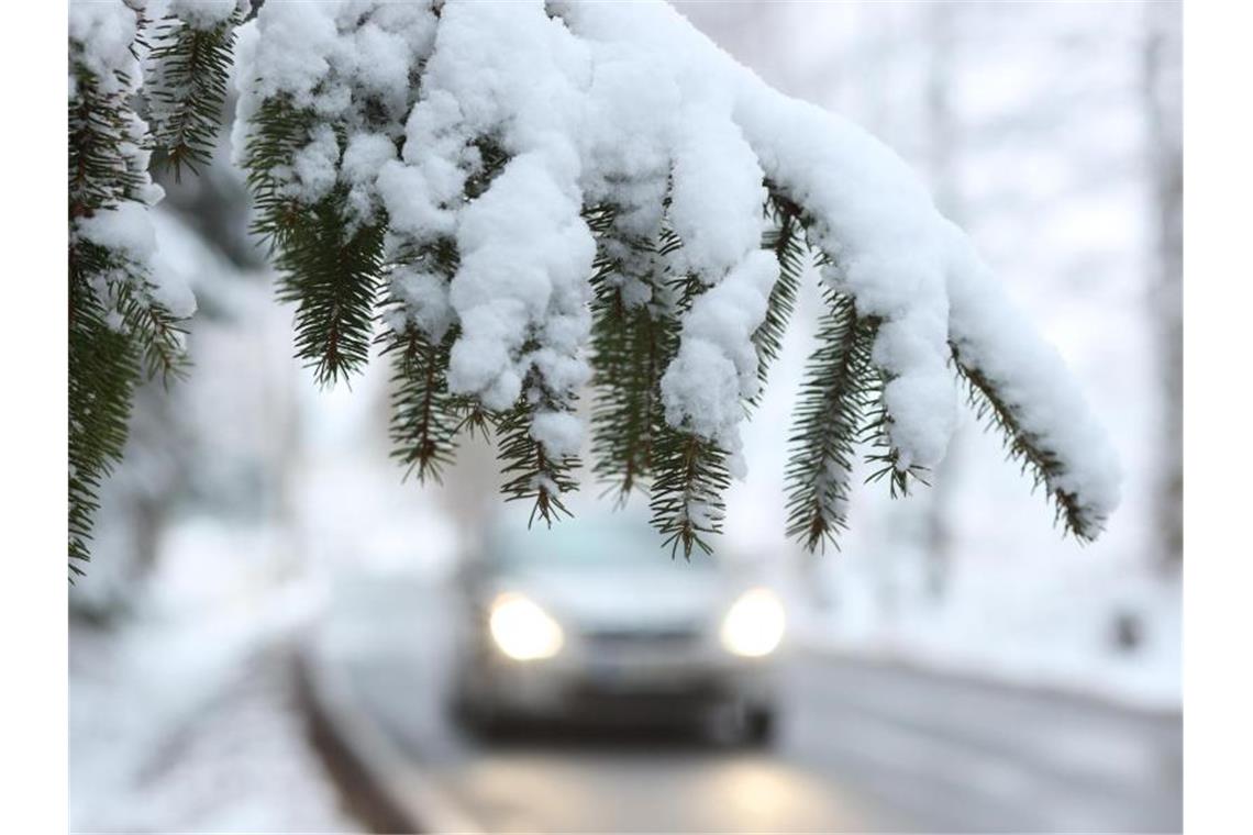 Ein Auto fährt hinter einem schneebedeckten Zweig über die Straße. Foto: Matthias Bein/dpa-Zentralbild/dpa/Symbolbild