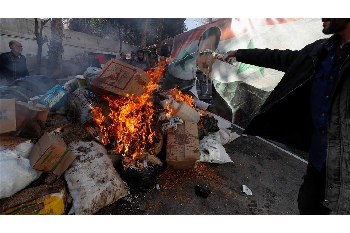 Ein Banner mit einem Bild des gestürzten syrischen Präsidenten Al-Assad verbrennt in Damaskus einem Feuer, in das ein syrisches Mitglied der Rebellenkräfte alkoholische Getränke gießt, um diese zu vernichten.