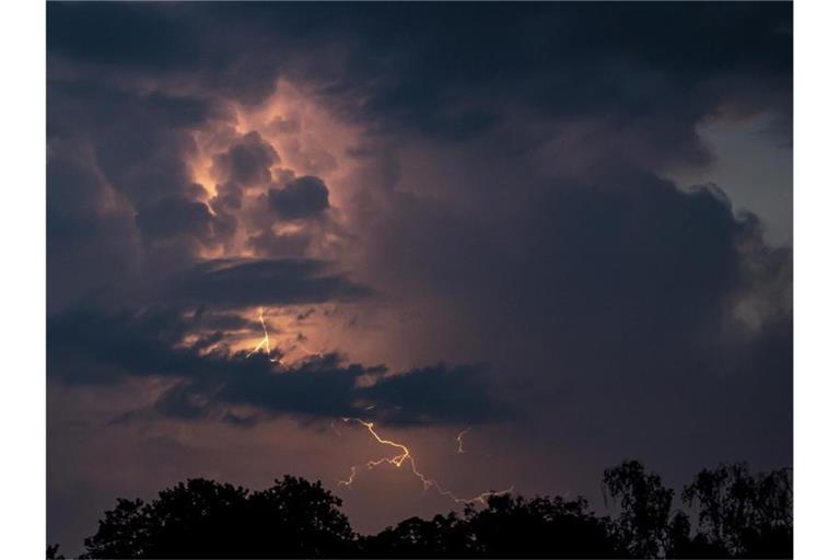 Ein Blitz hellt hinter dunklen Wolken auf. Foto: Fabian Sommer/dpa