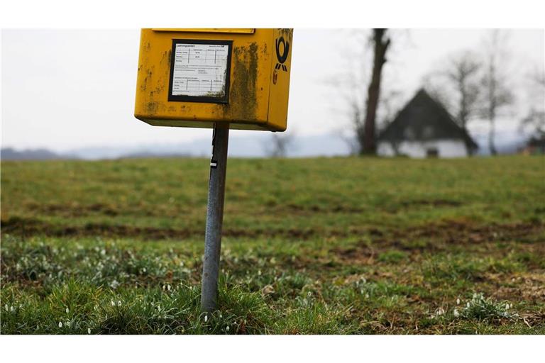 Ein Briefkasten der Deutschen Post steht auf einer Wiese am Rand einer Siedlung im Bergischen Land (NRW).