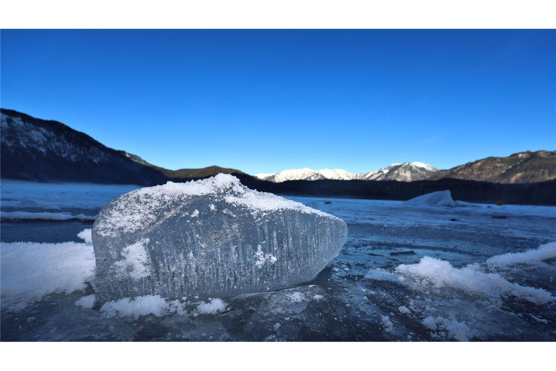 Ein Eisbrocken liegt auf dem mit einer Eisdecke überzogenen Eibsee.