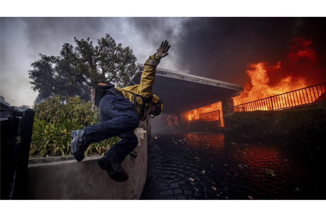 Ein Feuerwehrmann springt über einen Zaun, während er das Palisades-Feuer im Stadtteil Pacific Palisades bekämpft.