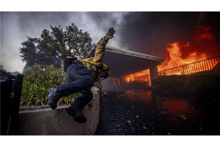 Ein Feuerwehrmann springt über einen Zaun, während er das Palisades-Feuer im Stadtteil Pacific Palisades bekämpft.