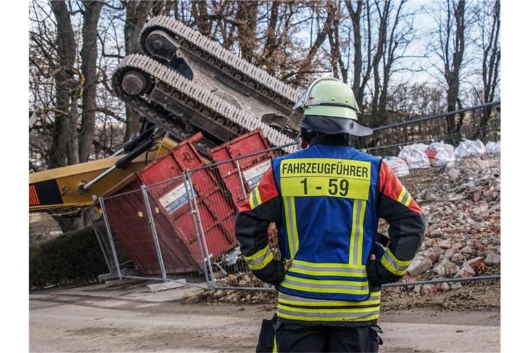 Ein Feuerwehrmann steht vor einem umgekippten Bagger. Foto: Dettenmeyer/SDMG/dpa