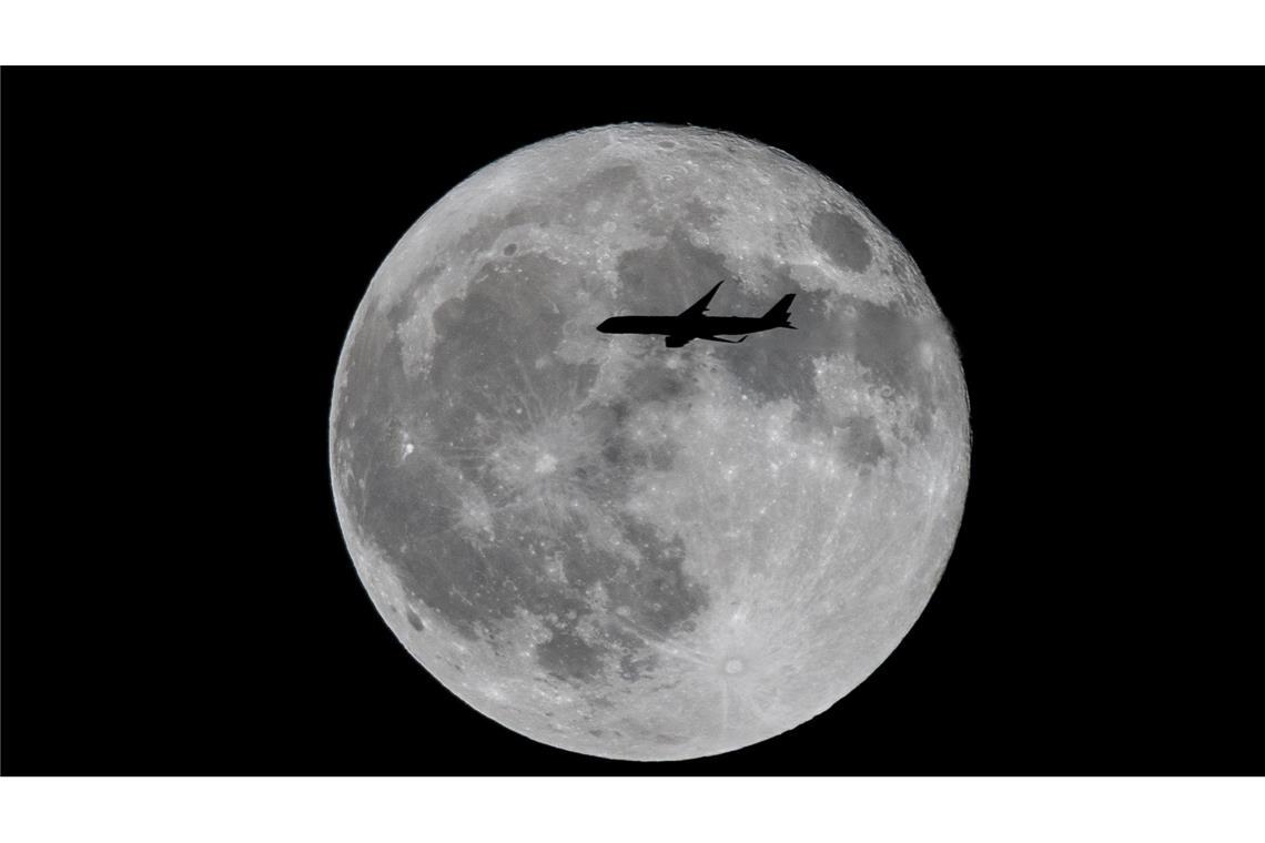 Ein Flugzeug fliegt an einem großen Vollmond vorbei.