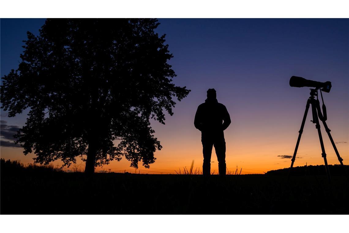 Ein Fotograf steht nach dem Sonnenuntergang mit seiner Ausrüstung auf einem Feld und wartet auf den Kometen Tsuchinshan-Atlas (Aufnahme mit Selbstauslöser).