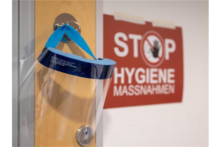 Ein Gesichtsschutz hängt neben einem Schild mit der Aufschrift „Stop Hygienemaßnahmen“. Foto: Sebastian Gollnow/dpa