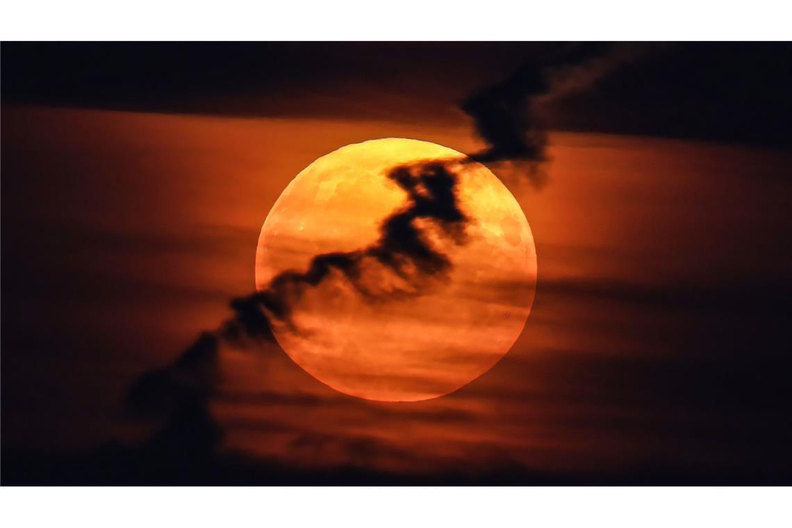 Ein großer Vollmond erscheint hinter Wolken am roten Abendhimmel. Da er näher an der Erde ist als sonst und damit größer erscheint, wird er als Supermond bezeichnet.