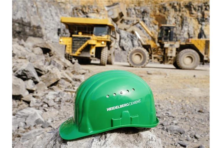 Ein grüner Schutzhelm mit der Aufschrift „HeidelbergCement“ liegt im Steinbruch des Baustoffkonzerns. Foto: Uwe Anspach/dpa/Archivbild