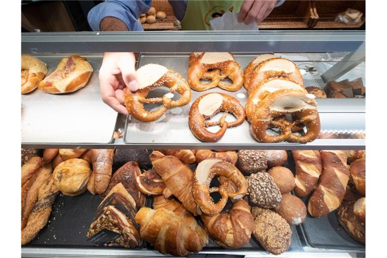 Ein Hand nimmt in einer Bäckerei eine Brezel aus einer Auslage. Foto: Bernd Weissbrod/dpa/Symbolbild