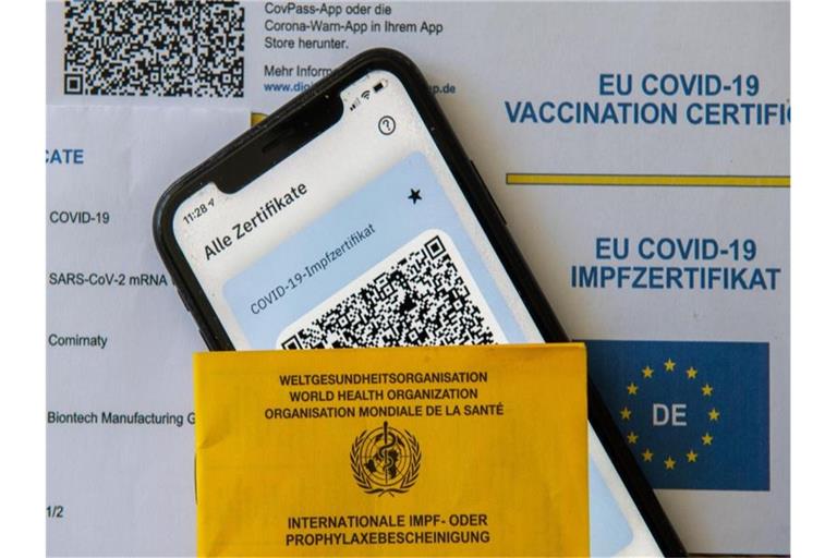 Ein Impfpass und ein Smartphone mit der CovPass-App liegen auf einem Impfzertifikat. Foto: Stefan Puchner/dpa/Symbolbild