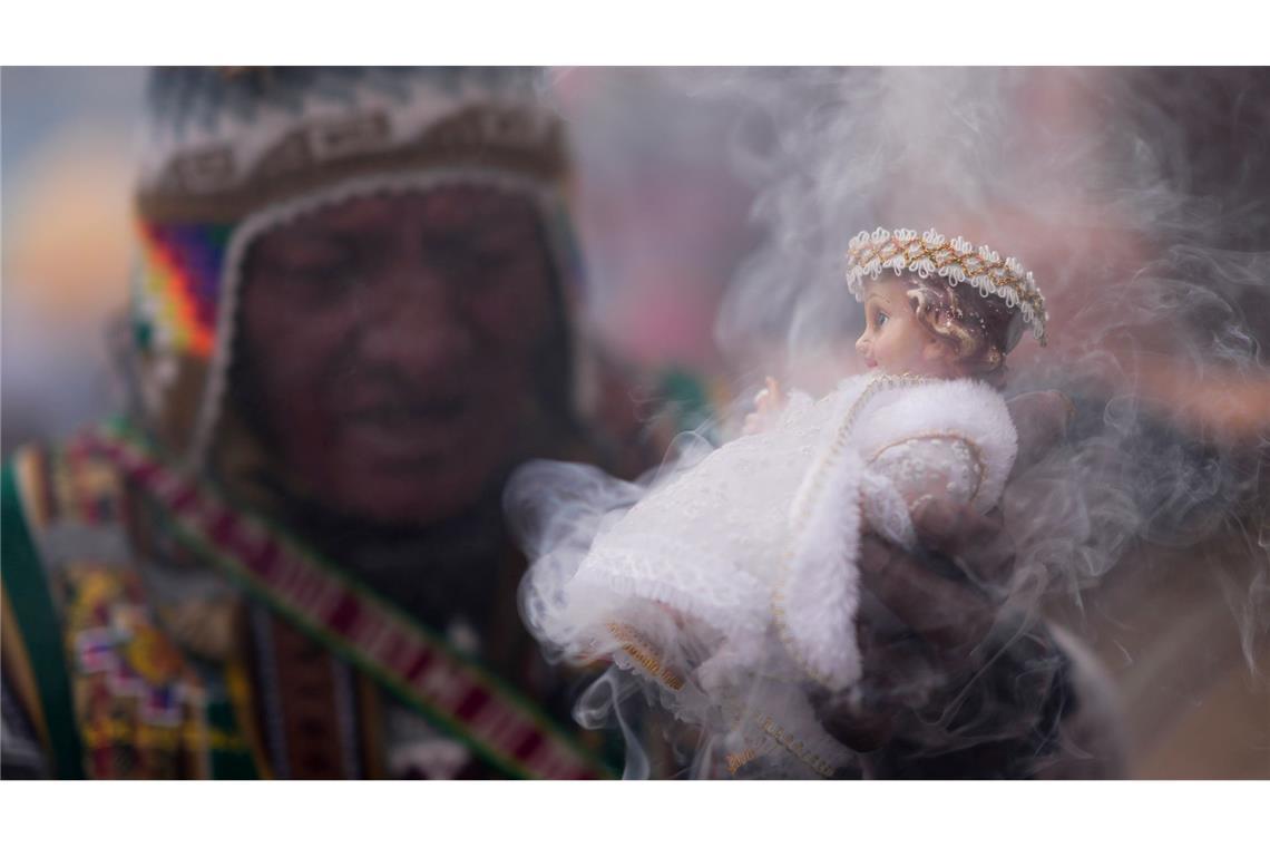 Ein indigener spiritueller Führer der Aymara segnet eine Statue des Jesuskindes mit Weihrauch nach einem Dreikönigsgottesdienst in einer katholischen Kirche in Bolivien.