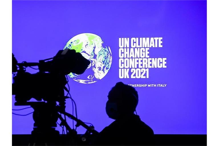 Ein Kameramann steht bei der Weltklimakonferenz in Glasgow vor einem Bildschirm, der das Logo der Konferenz zeigt. Foto: Christoph Soeder/dpa/Archivbild