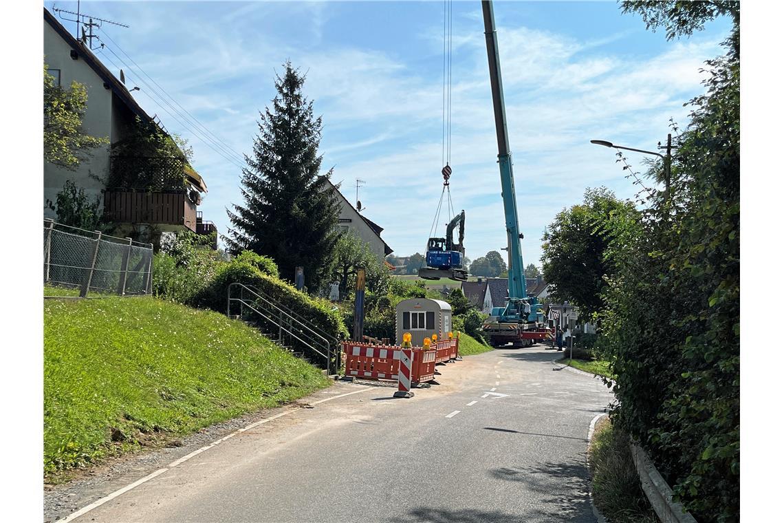 Ein Klein-Bagger wird von einem Autokran über die Häuser in die Gärten gehievt. ...