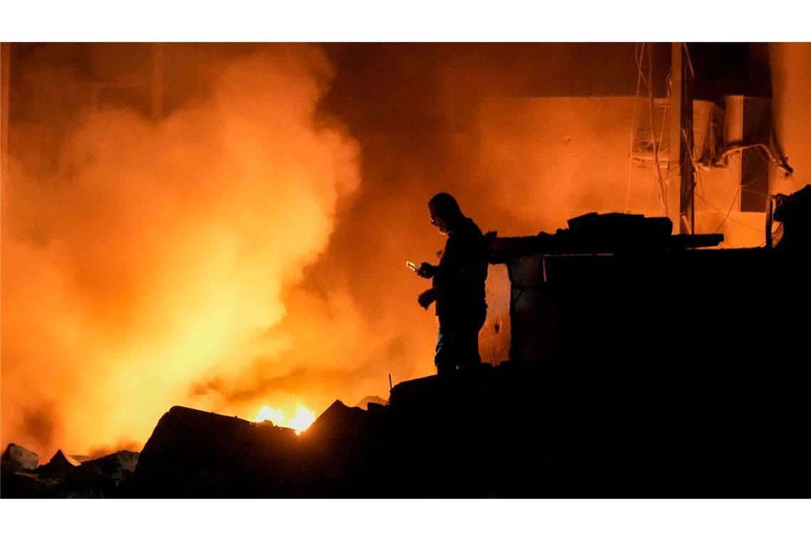 Ein Mann benutzt sein Mobiltelefon, während Flammen und Rauch von Gebäuden nach einem israelischen Luftangriff im Zentrum von Beirut aufsteigen.