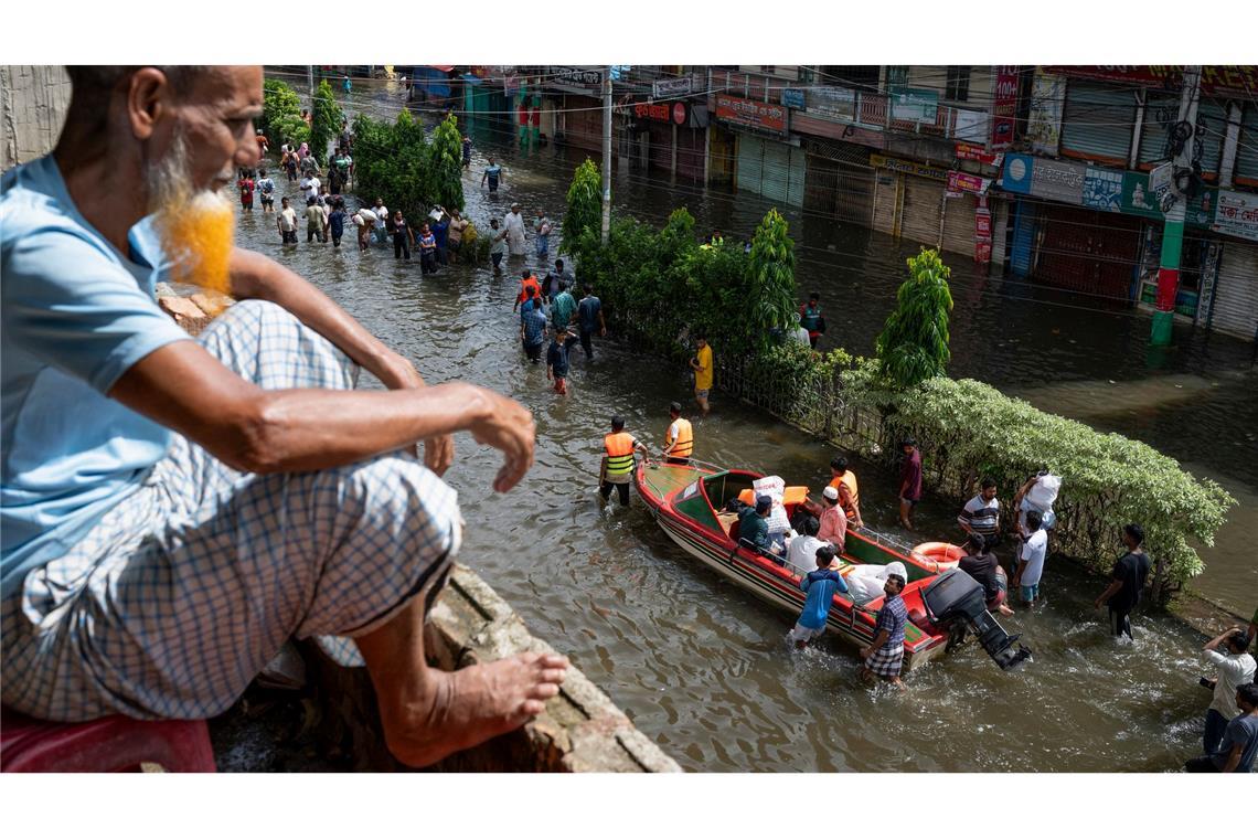 Ein Mann beobachtet von einem Balkon aus, wie Menschen ihre Habseligkeiten auf einem Boot durch eine überschwemmte Straße in Feni, im Südosten von Bangladesch, fahren. Schwere Regenfälle haben große Gebiete in Bangladesch überflutet.