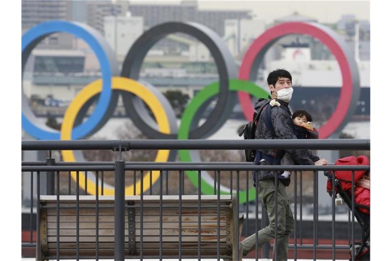 Ein Mann läuft an den Olypischen Ringen vorbei. Foto: Koji Sasahara/AP/dpa/Archivbild