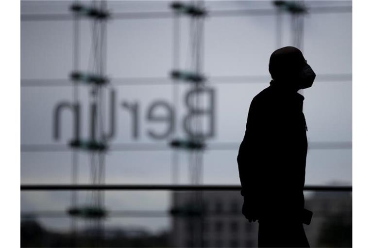 Ein Mann mit Mund-Nasen-Schutz im Berliner Hauptbahnhof vor dem „Berlin“-Schriftzug. Foto: Christoph Soeder/dpa