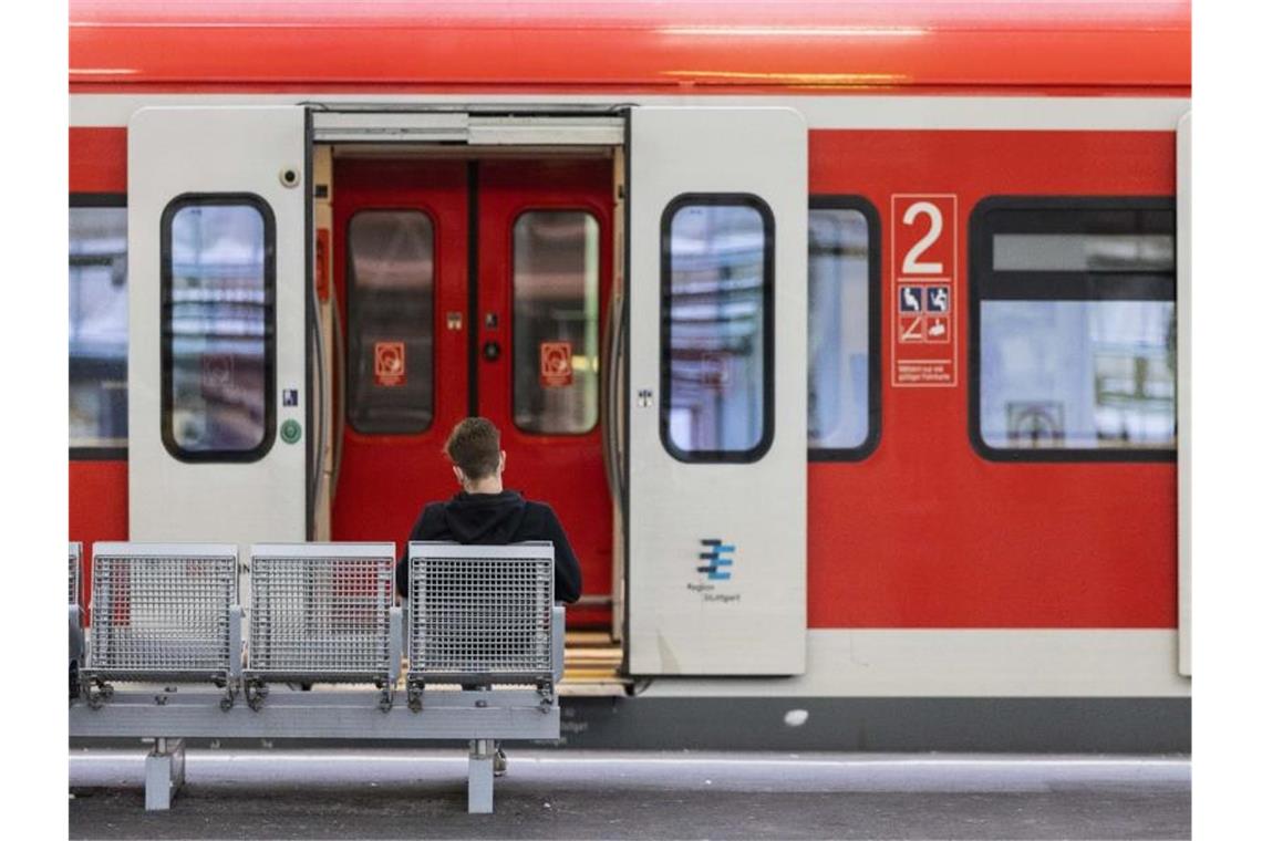 Ein Mann sitzt an einem Bahnhof vor einem Regionalzug auf der Bank. Foto: Tom Weller/dpa/Symbolbild