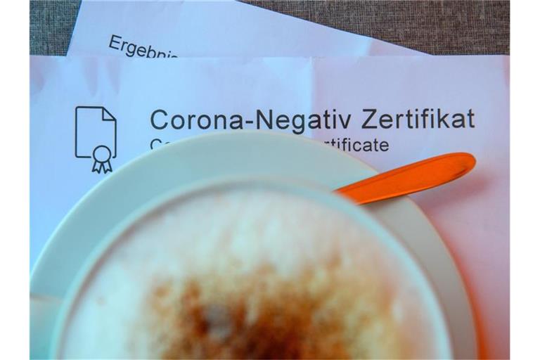 Ein Milchkaffee steht in einem Café auf einem Tisch auf einem Corona-Negativ Zertifikat. Foto: Klaus-Dietmar Gabbert/dpa-Zentralbild/dpa/Symbolbild