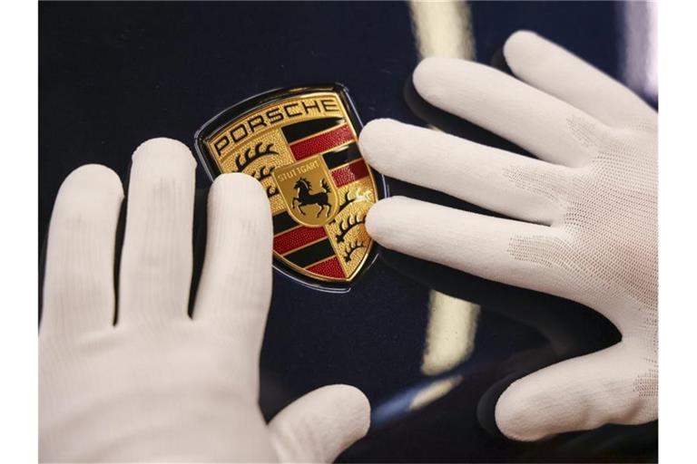 Ein Mitarbeiter befestigt das Wappen an einem Porsche Macan im Leipziger Porsche Werk. Foto: Jan Woitas/dpa-Zentralbild/dpa/Symbolbild