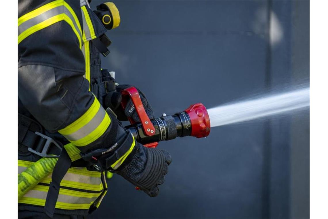 Ein Mitglied der Feuerwehr spritzt aus einem Schlauch mit Wasser. Foto: David Inderlied/dpa/Symbolbild