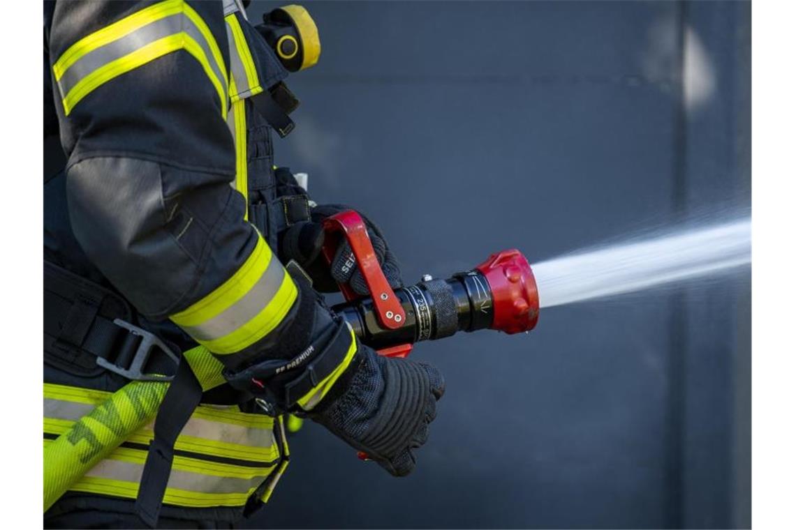 Kellerbrand löst Großeinsatz aus Ein Mitglied der Feuerwehr spritzt aus einem Schlauch mit Wasser. Foto: David Inderlied/dpa/Symbolbild