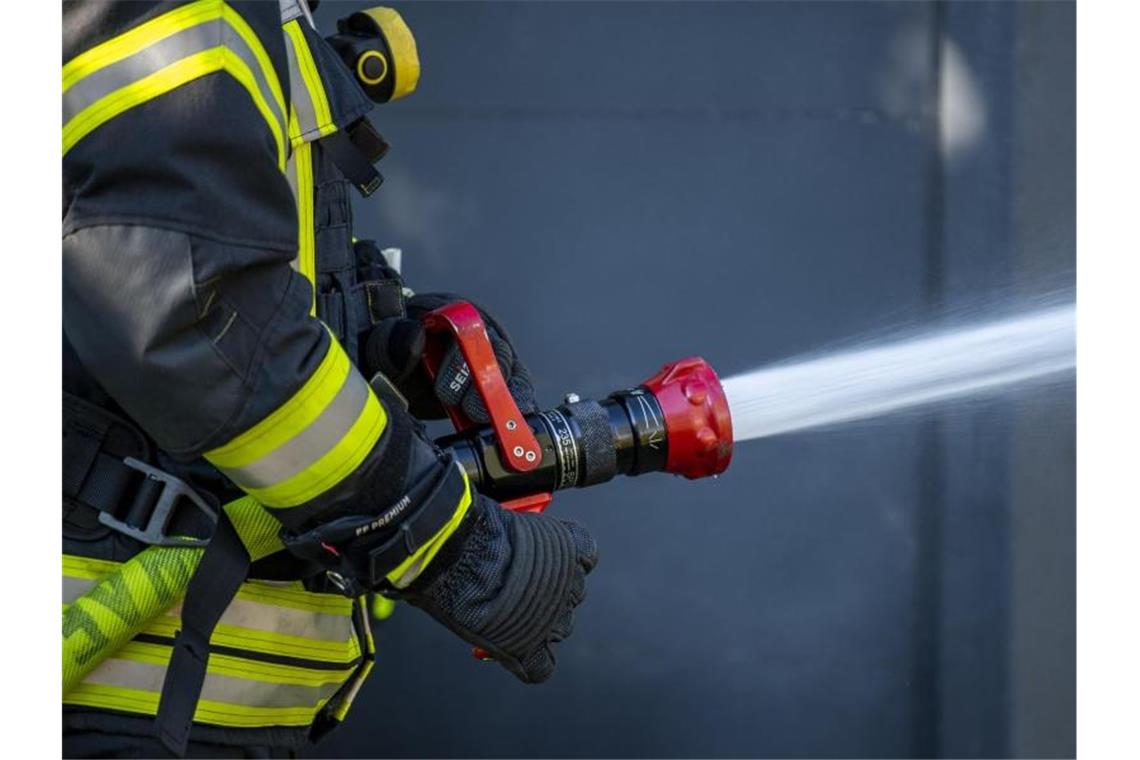 Brennender Holzstapel verursacht Feuer in Wohnhaus Ein Mitglied der Feuerwehr spritzt aus einem Schlauch mit Wasser. Foto: David Inderlied/dpa/Symbolbild