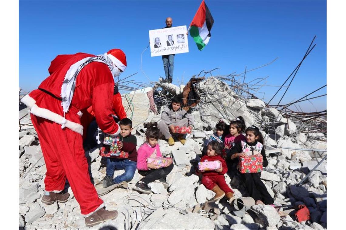 Christen in aller Welt feiern Weihnachten Ein Palästinenser im Weihnachtsmannkostüm verteilt Geschenke und Süßigkeiten an Kinder, die auf den Überresten zerstörter Häuser sitzen. Foto: Abedalrahman Hassan/APA Images via ZUMA Wire/dpa